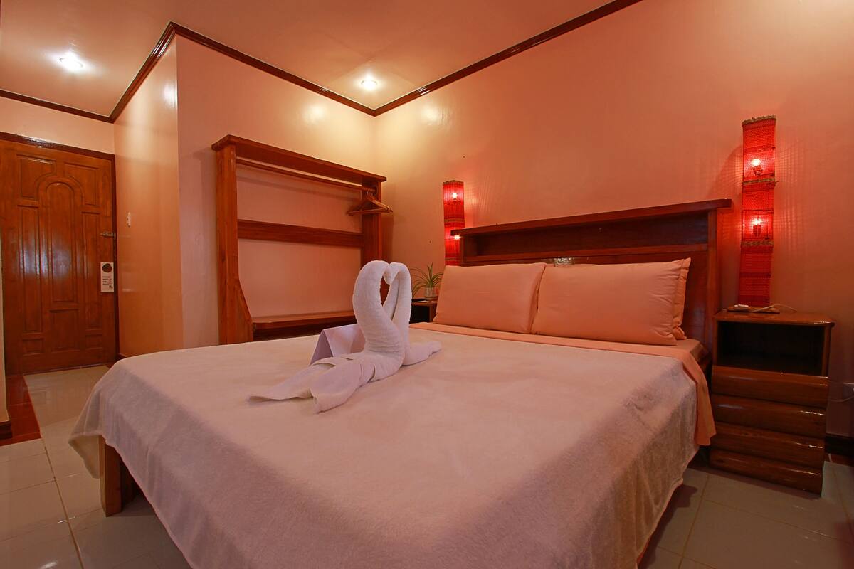 A hotel room with a large bed, a wooden headboard, a nightstand, and a red decorative light.