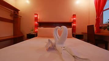 A hotel room with a neatly made bed, a wooden headboard, a bedside table with a lamp, and a red curtain.