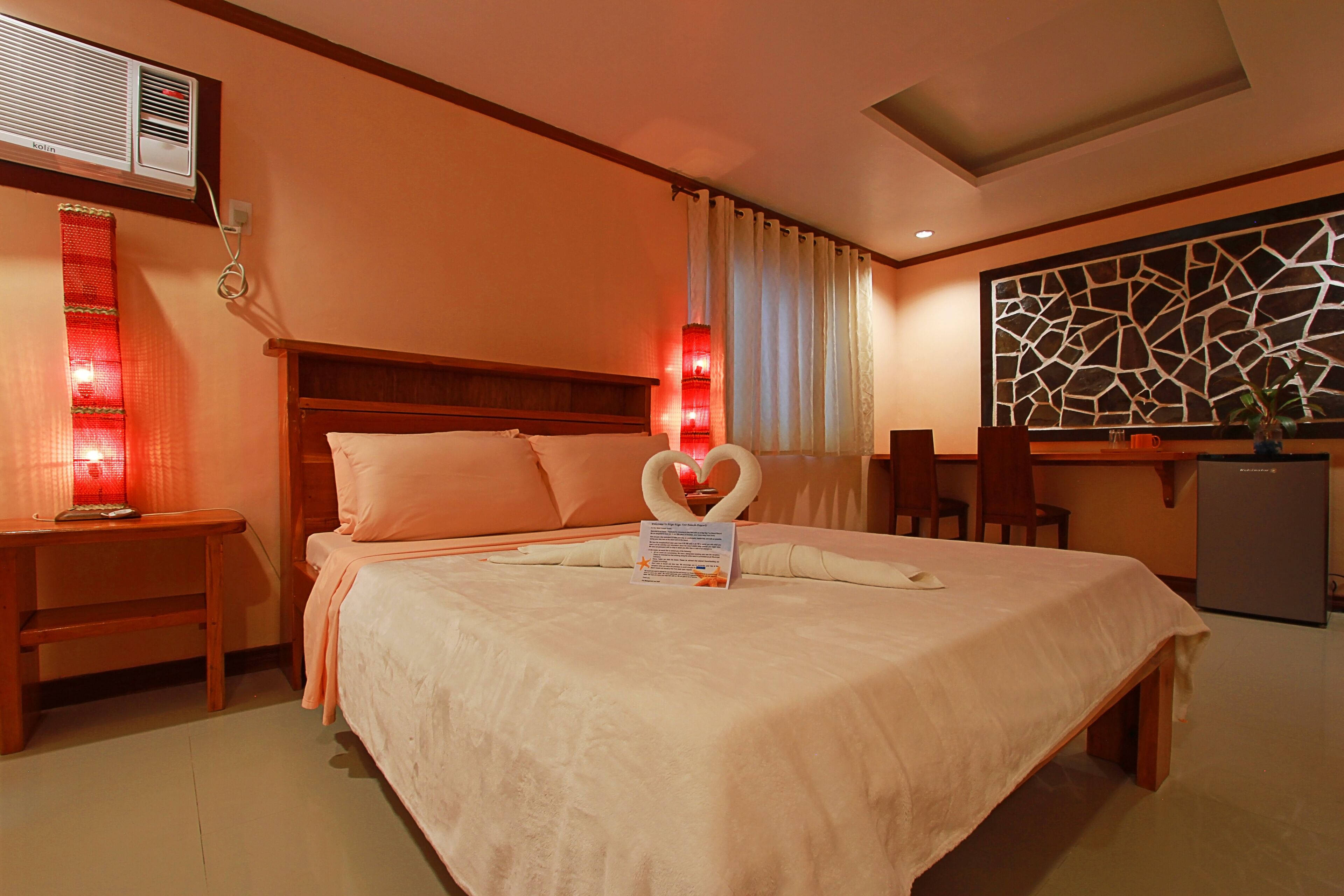 A hotel room with a bed, a desk, a chair, a small refrigerator, and a decorative wall piece.