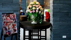 A modern interior with a dark brick wall, a chandelier, a round table with chairs, and a floral arrangement. - Mayflower Grande Hotel Chiang Mai (Chiang Mai)