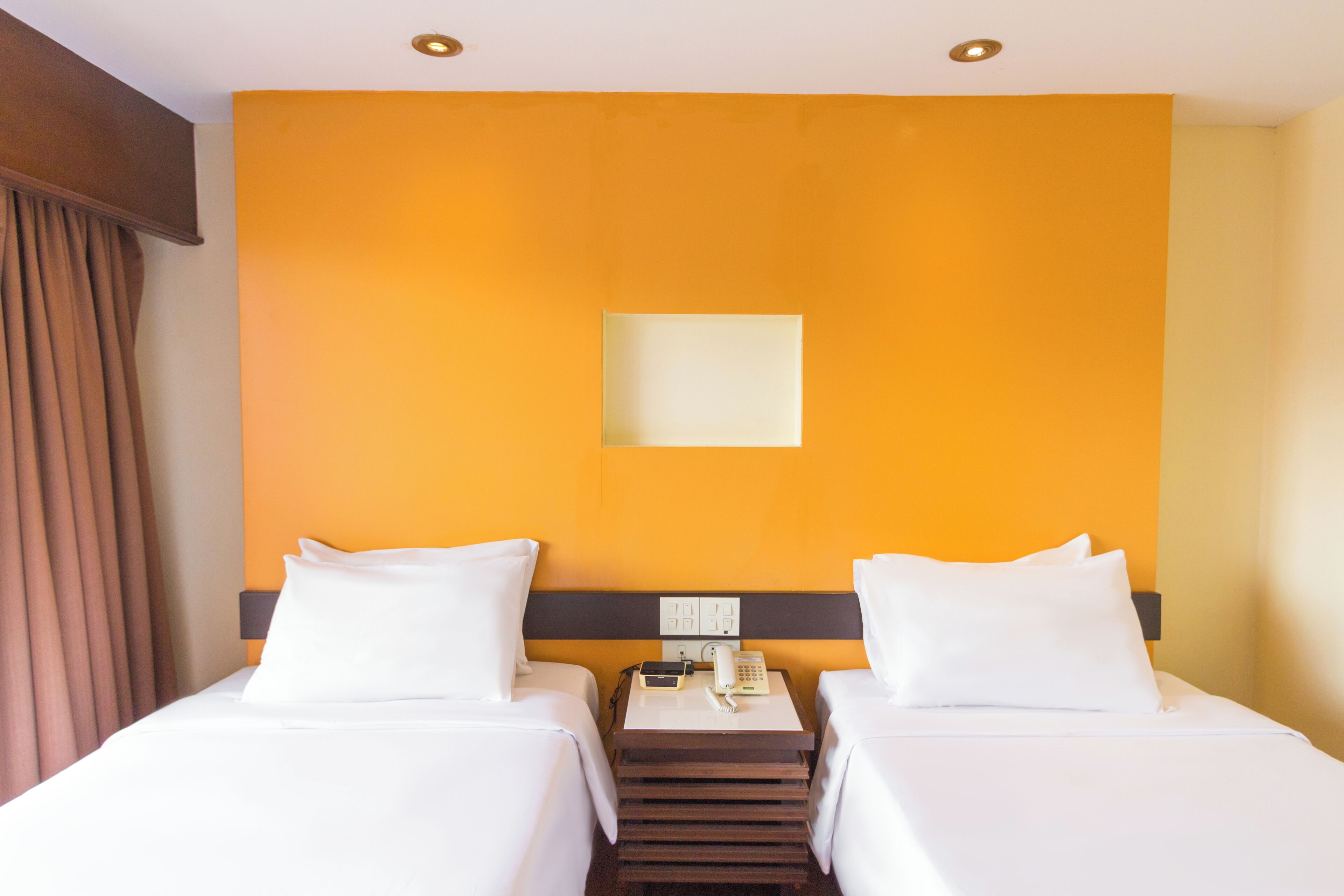 Une chambre d’hôtel avec deux lits, une table de chevet avec un téléphone et une lampe, et un interrupteur fixé au mur.
