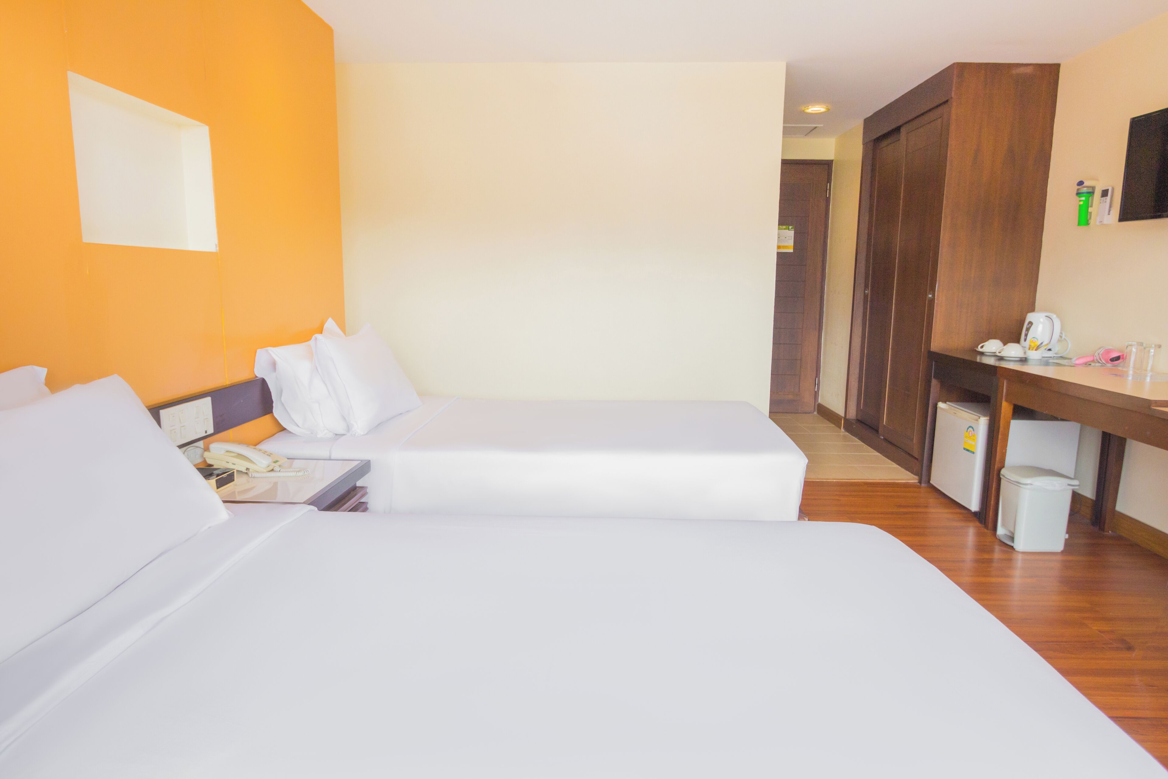 A hotel room with two beds, a desk, a chair, a television, and a wardrobe.