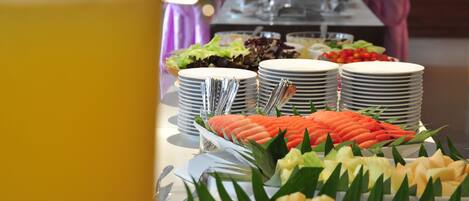 A buffet table with various food items and stacked plates.