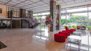 A spacious lobby with a staircase, red seating, and a large window offering a view of greenery. - Mayflower Grande Hotel Chiang Mai (Chiang Mai)
