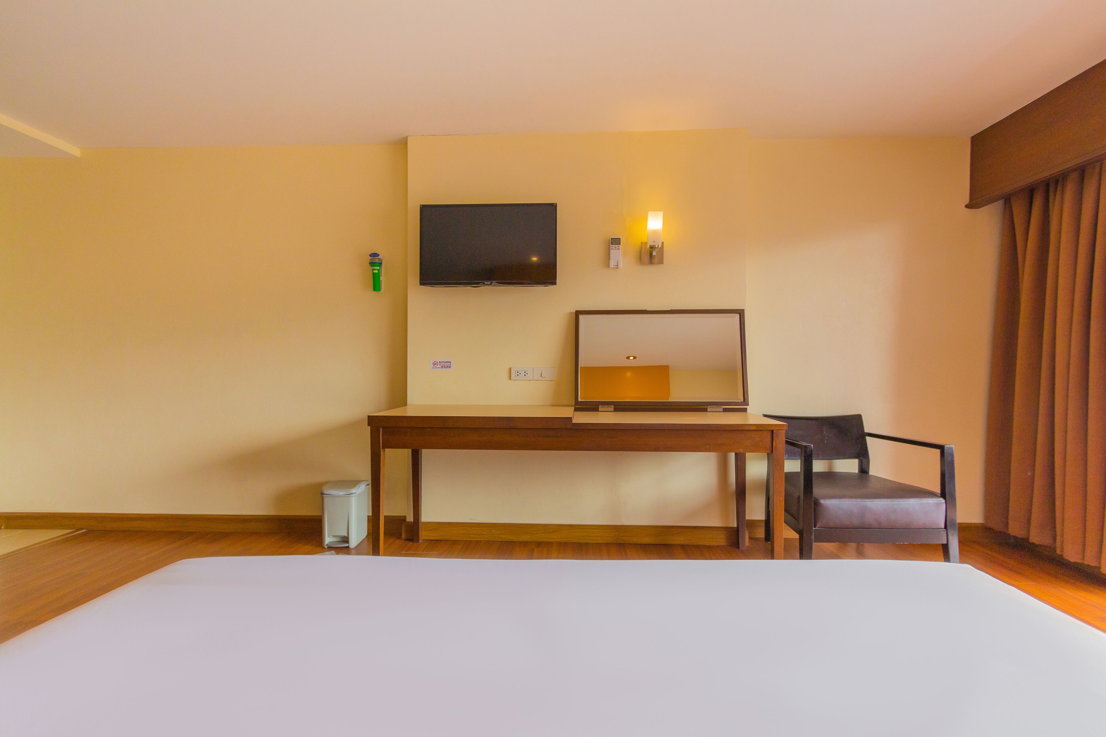 A hotel room with a bed, a desk, a chair, a television, and a wall-mounted light.