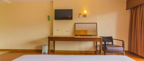 A hotel room with a bed, a desk, a chair, a television, and a wall-mounted light.