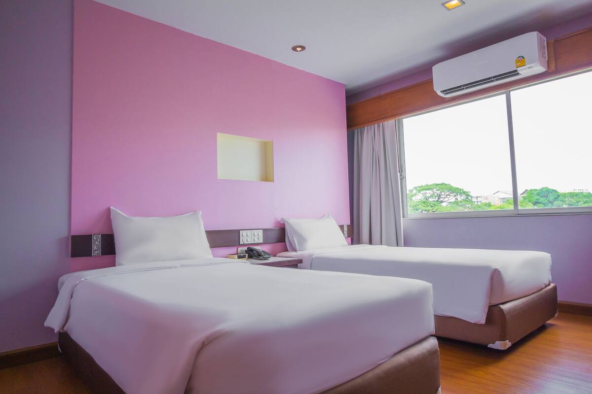 Une chambre d’hôtel avec deux lits, une grande fenêtre donnant sur un beau paysage, un appareil de climatisation et une table de chevet avec un téléphone.