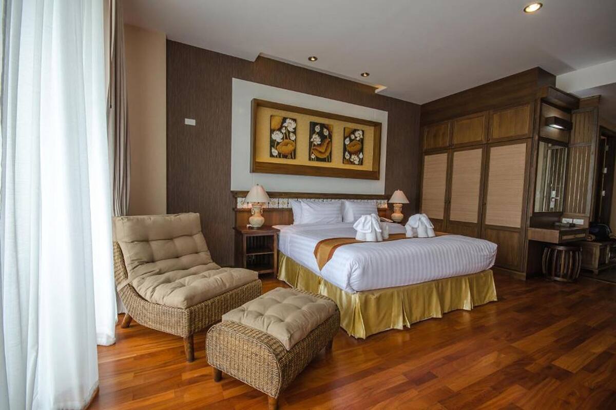 Een hotelkamer met een bed, twee nachtkastjes, een stoel, een poef, een groot schilderij en een garderobe.