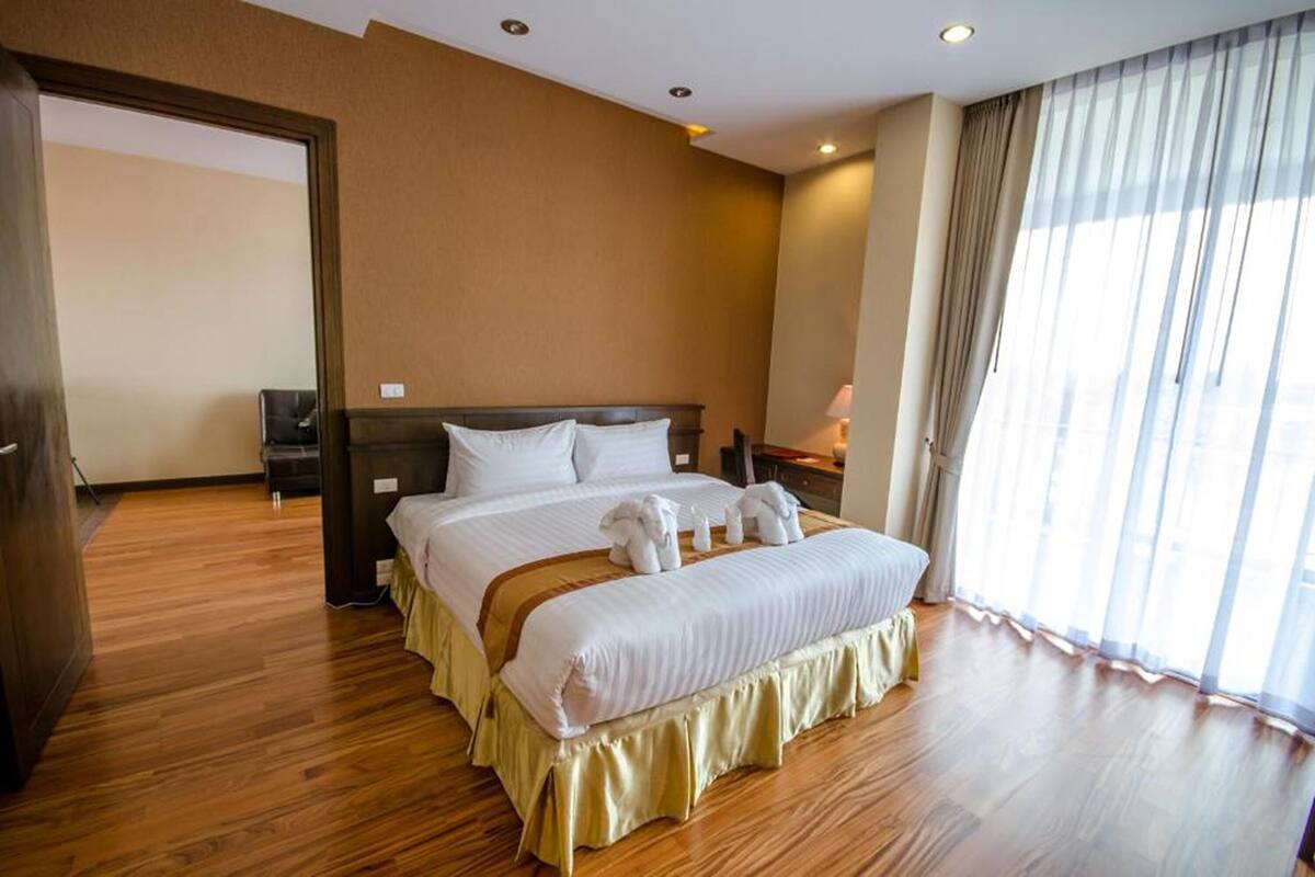 Een hotelkamer met een groot bed, houten vloeren, een nachtkastje en een raam met gordijnen.