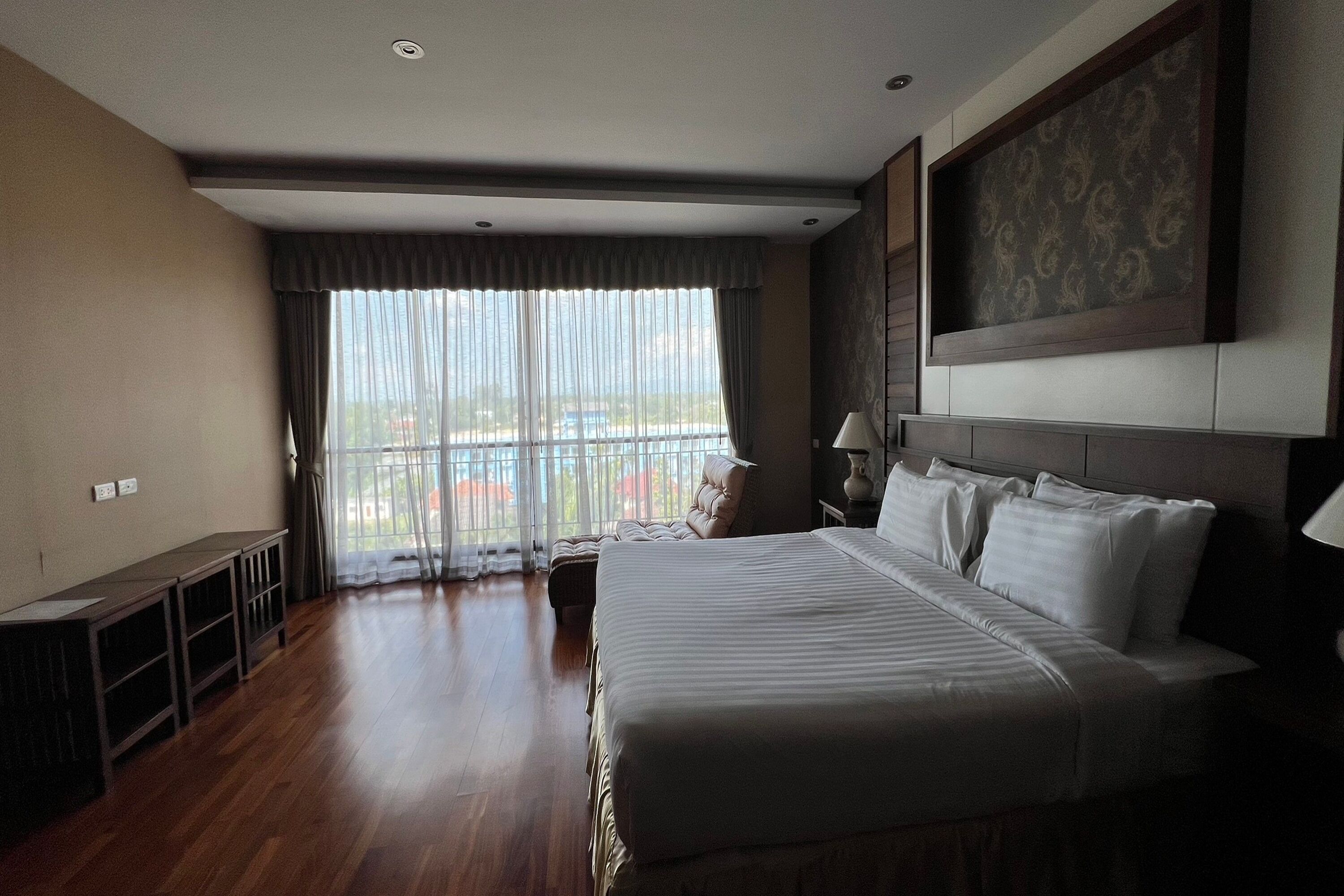 Habitación de hotel con una cama grande, un escritorio y vistas al exterior a través de cortinas translúcidas.