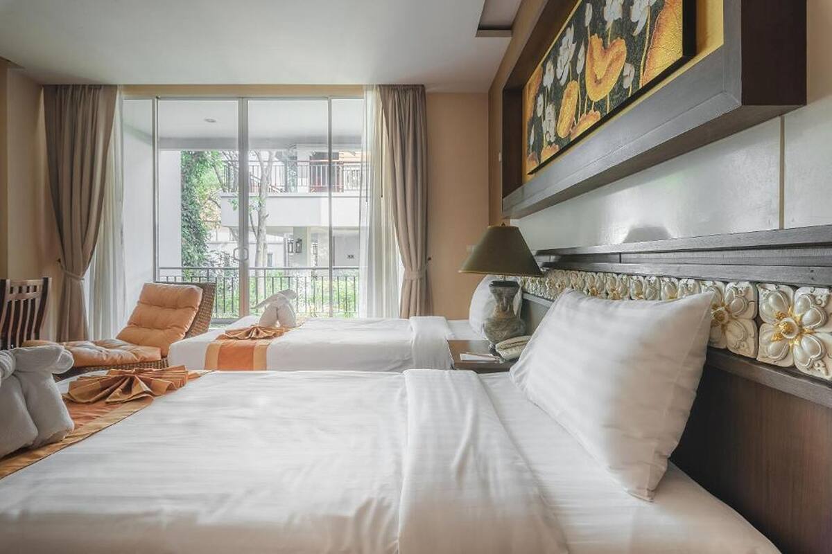 Een hotelkamer met twee bedden, een zithoek met een fauteuil, een lamp en een schilderij aan de muur.