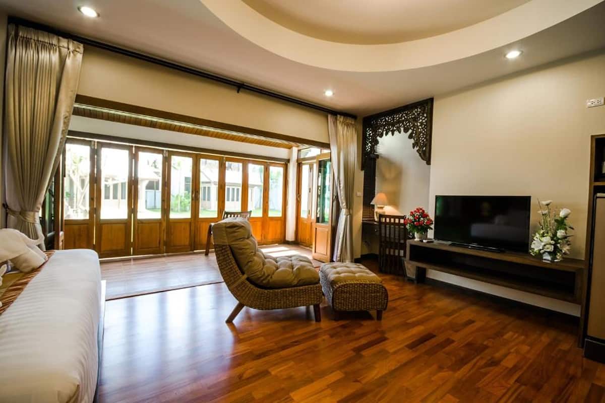Een ruime woonkamer met een groot raam, een comfortabele bank, een rieten fauteuil, een tv op een houten dressoir en een decoratief wandkunstwerk.