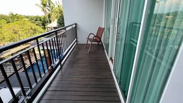 Un balcón con piso de madera, una silla y vista a una piscina y follaje.