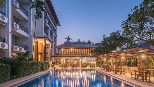 Un hotel con piscina, mobiliario exterior y un edificio con varios balcones.