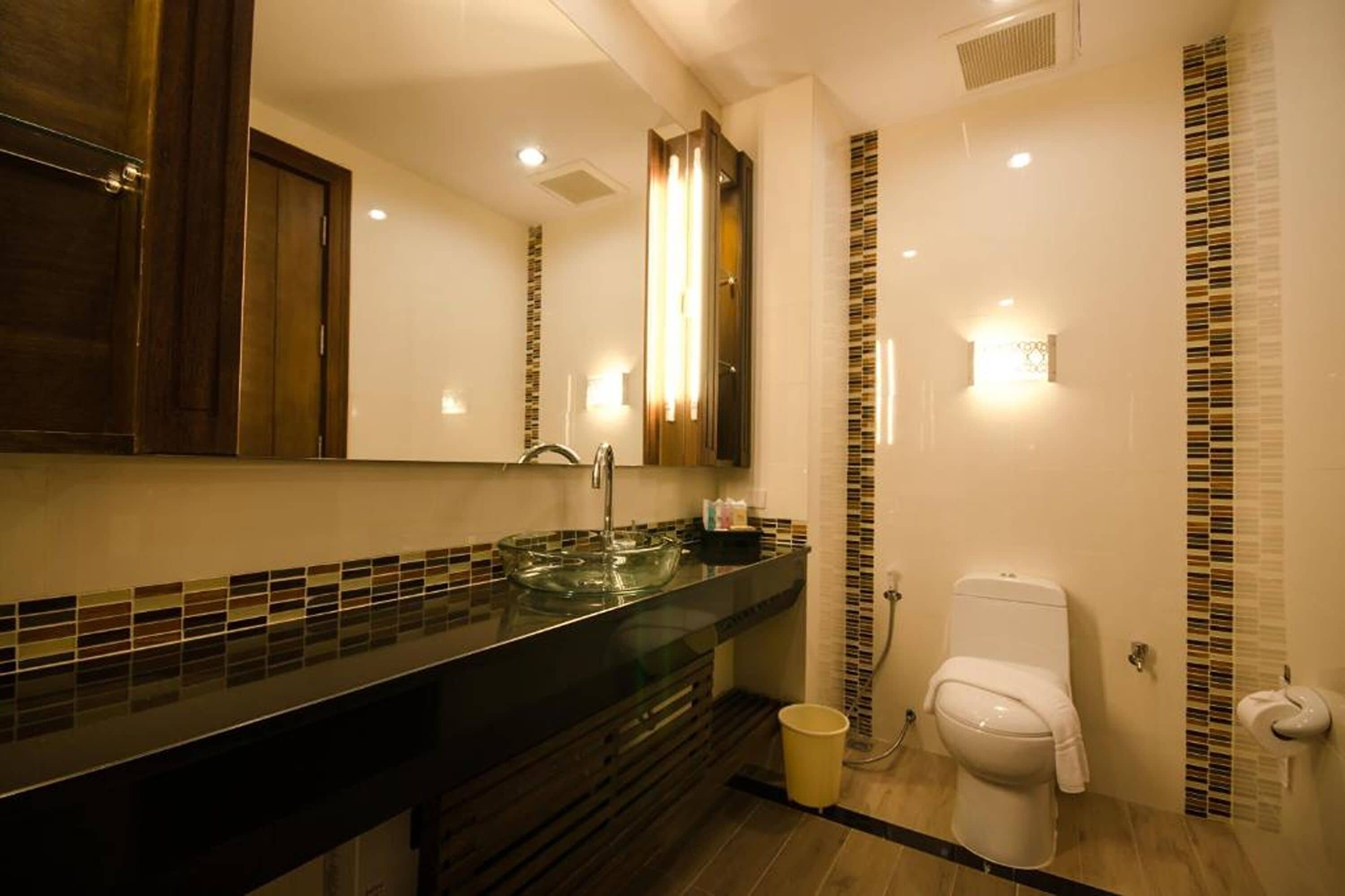 Ein modernes Badezimmer mit Waschbecken aus Glas, Toilette und Spiegel.
