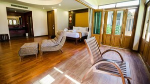 Una habitación amplia con una cama grande, dos sillas de mimbre y un banco de madera.