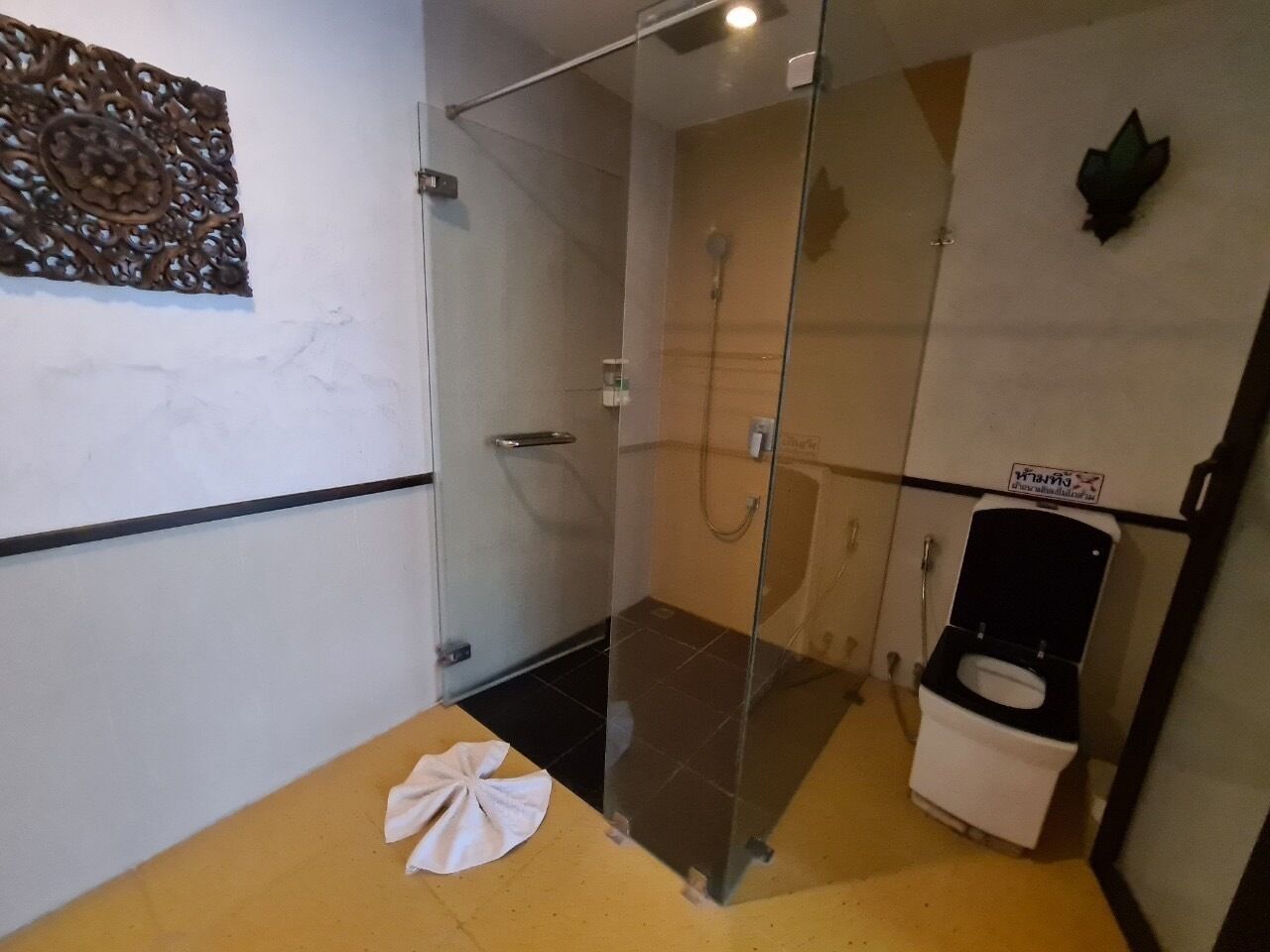 A bathroom with a glass shower enclosure, a white toilet, and a towel on the floor.