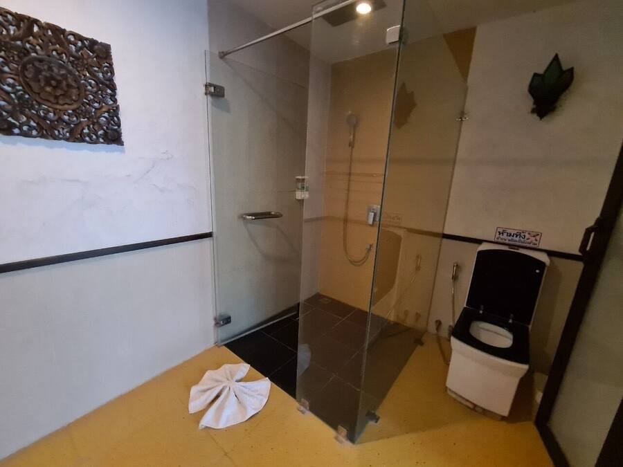 A bathroom with a glass shower enclosure, a white toilet, and a towel on the floor.