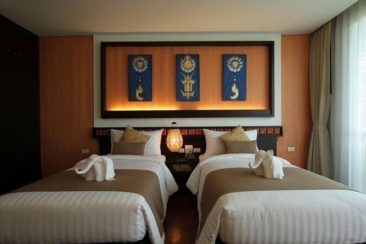 A hotel room with two beds, a decorative wall with three framed artworks, and a lamp on the nightstand.