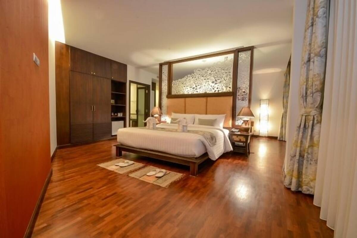 A spacious bedroom with a large bed, wooden wardrobe, and a mirror above the bed.