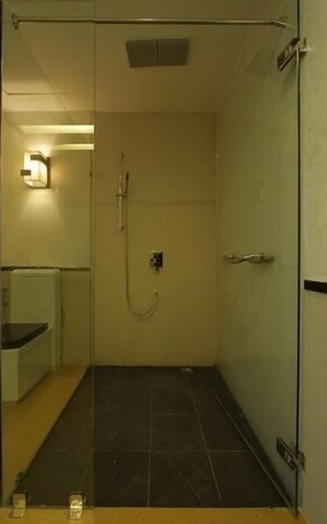 Un espacio de ducha pequeño y cerrado con puerta de vidrio, un perchero y una lámpara en la pared.