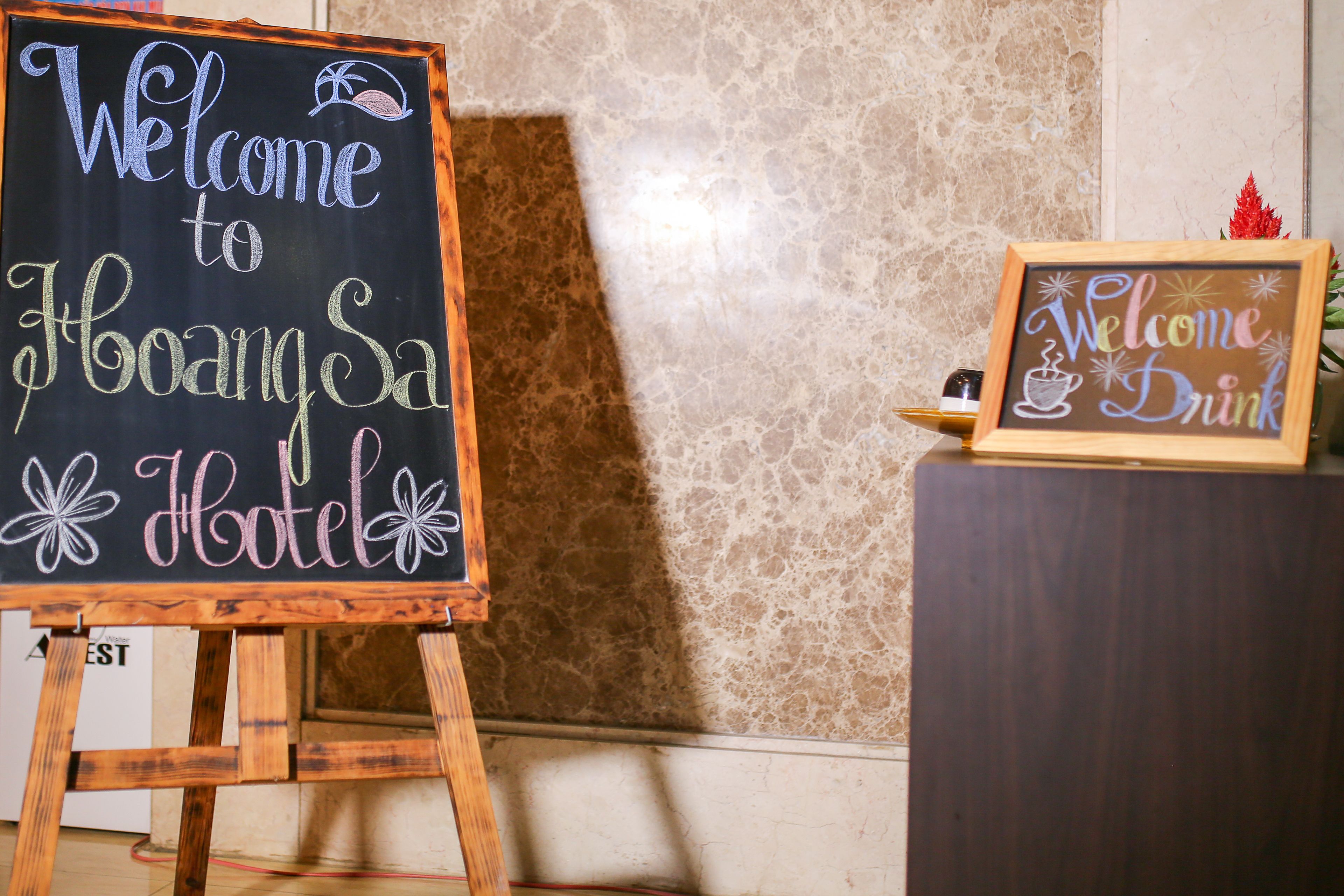 A chalkboard sign welcoming guests to a hotel, a framed sign with a coffee cup, and a wooden stand.