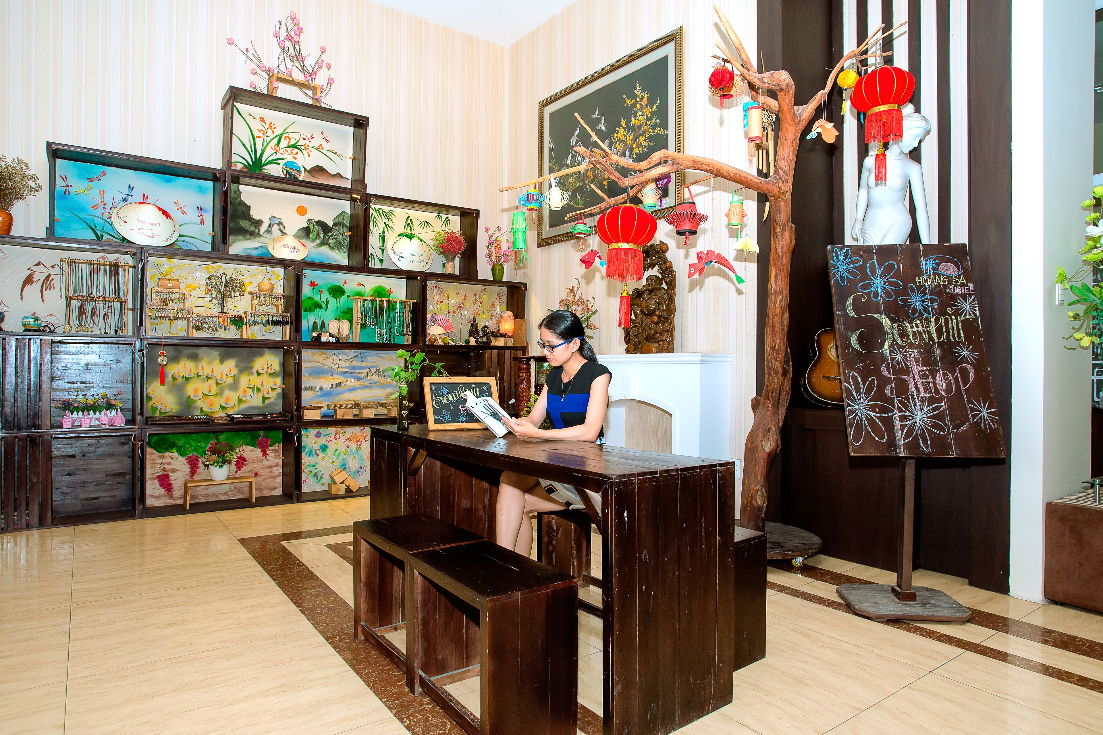 A room with a wooden desk, a chair, and a person reading a magazine. There are shelves with various items and decorations.