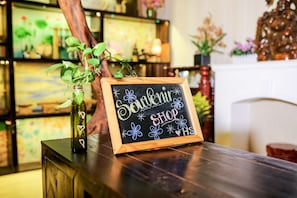 A chalkboard sign with "Souvenir Shop" written on it, placed on a wooden table with a plant beside it. - Hoang Sa Hotel (Da Nang)