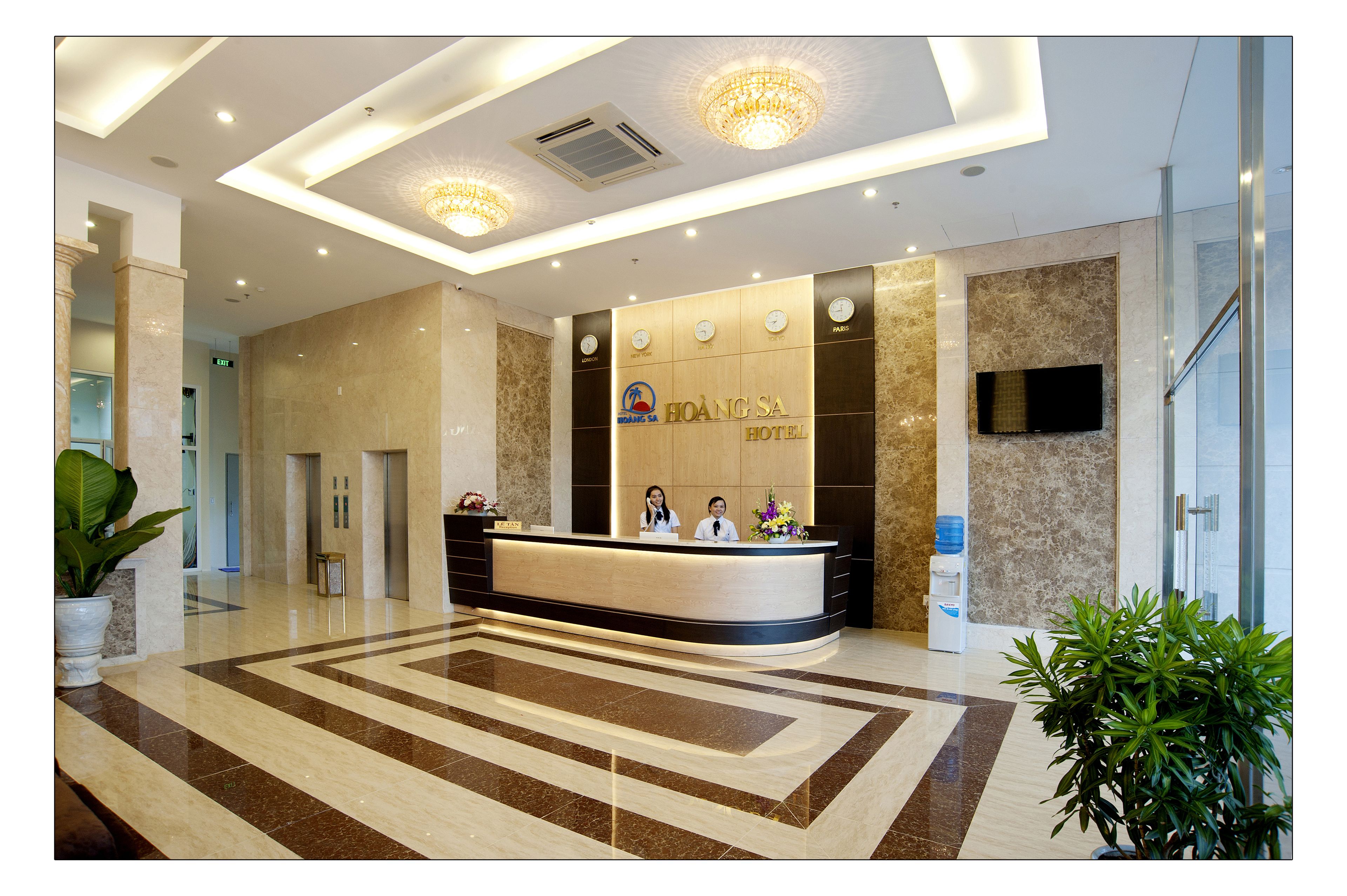 A hotel reception area with a marble reception desk, a flat-screen TV, and a large potted plant.