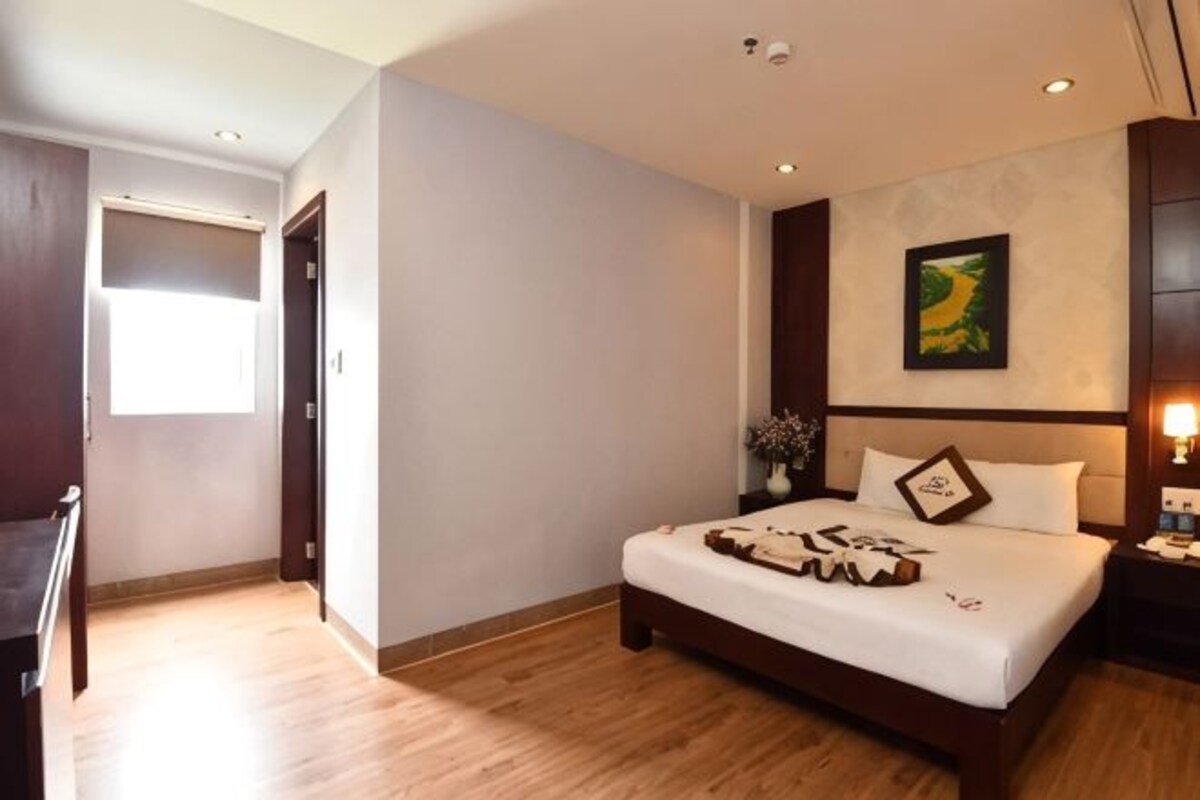 A hotel room with a bed, a nightstand, a wall-mounted artwork, and a window.