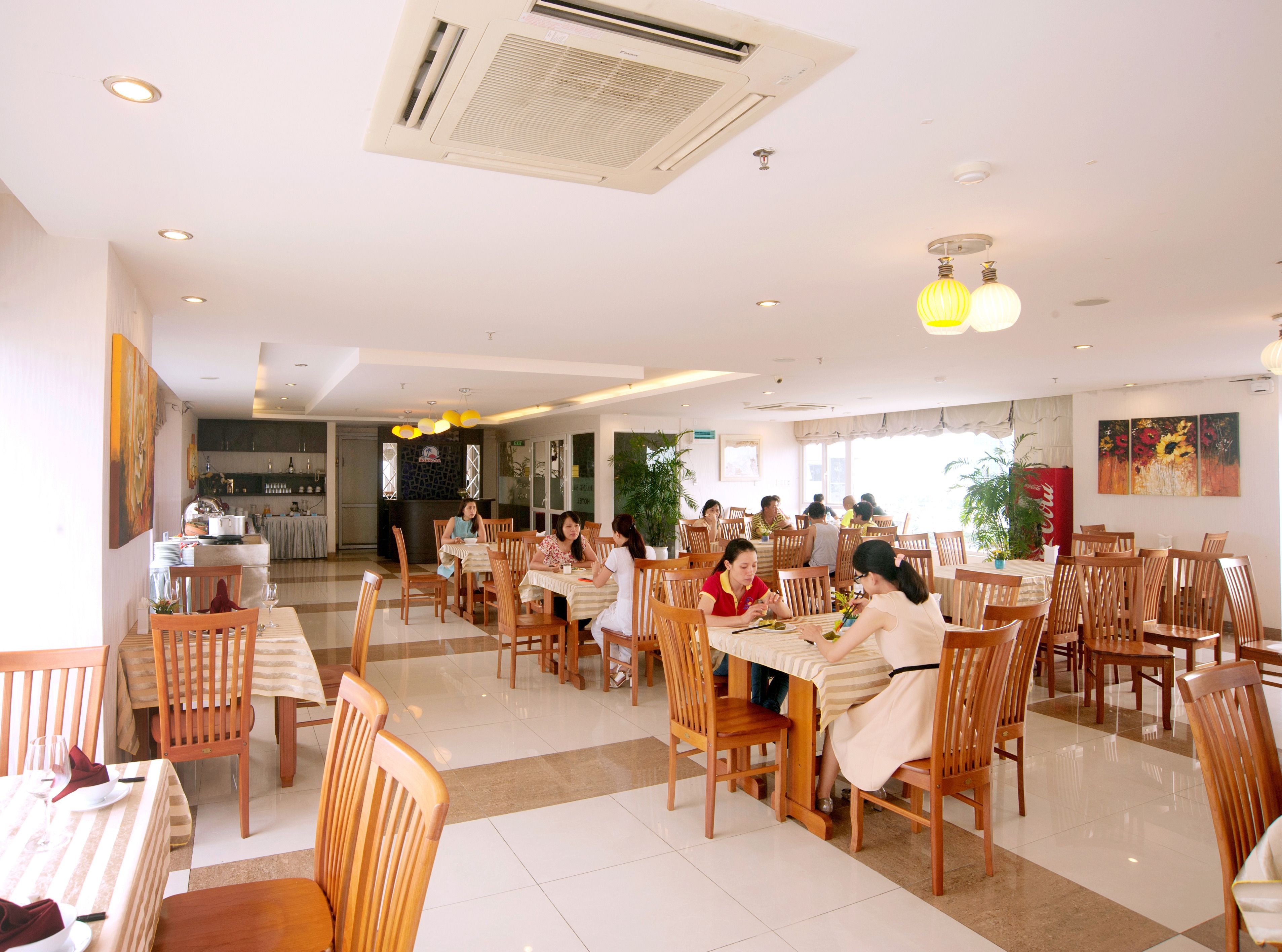 A spacious dining area with multiple tables and chairs, a kitchen in the background, and a bright, well-lit environment.