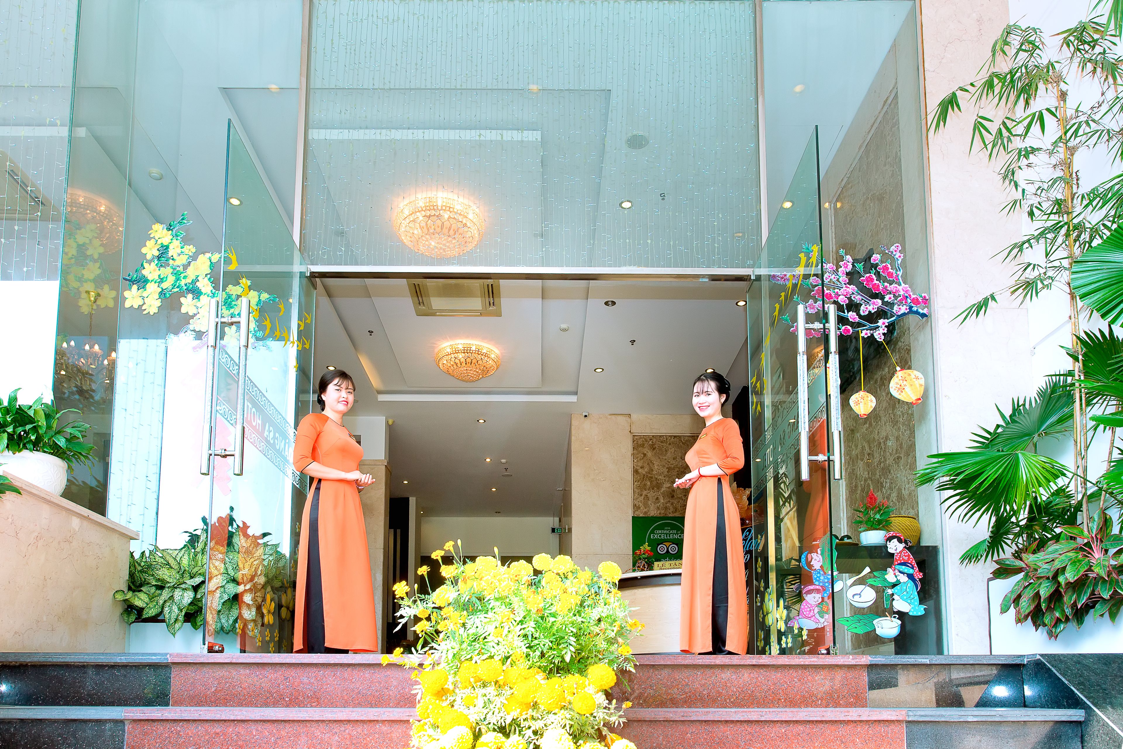 A hotel entrance with a glass facade, a reception desk, and a staircase leading to the lobby.