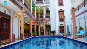 A pool area with a checkered floor, columns, and potted plants.
