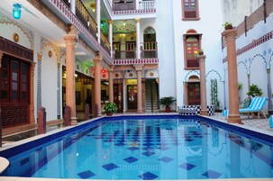 Uma área de piscina com piso quadriculado, colunas e plantas em vasos.