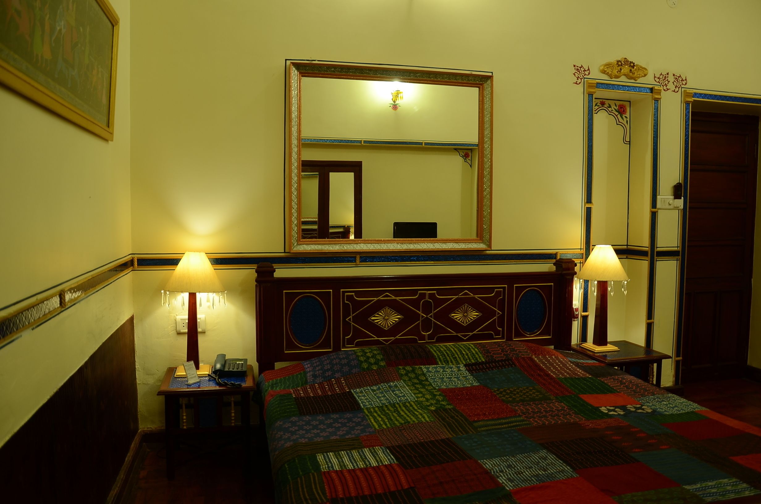 A hotel room with a large mirror, two bedside lamps, a quilted bedspread, and a wooden headboard.