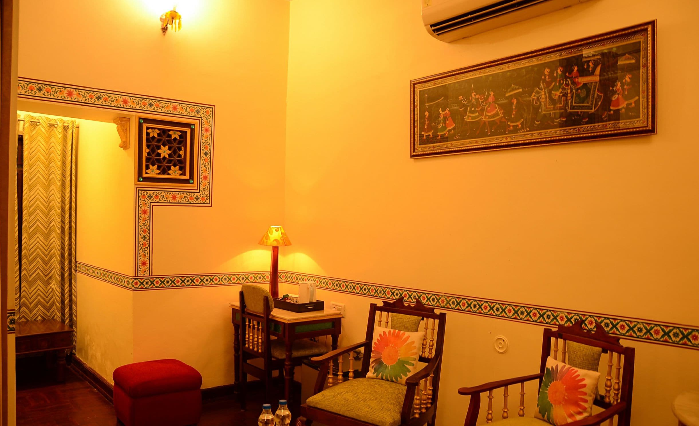 A room with a traditional design, featuring a patterned border along the walls, a wooden chair with a colorful cushion, and a framed artwork depicting a historical scene.
