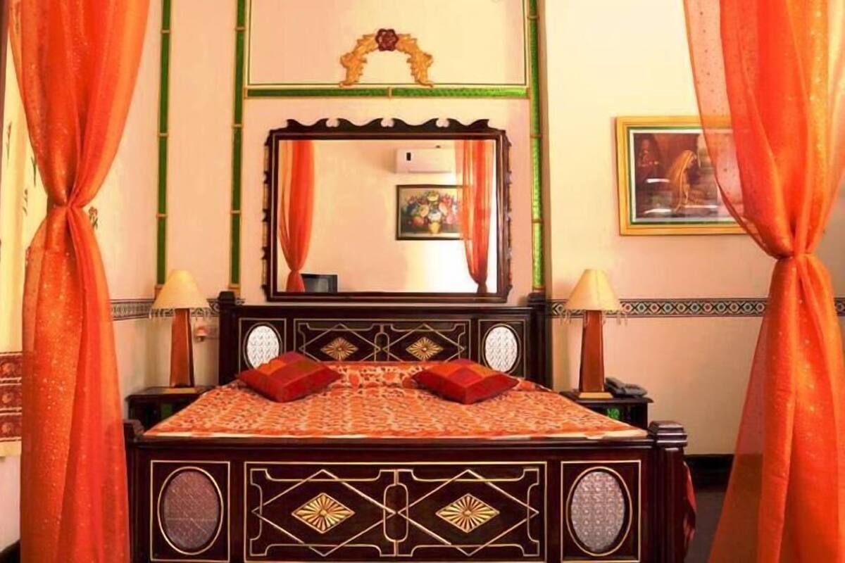 Una cama con una colcha estampada, dos almohadas, un espejo sobre la cama y dos lámparas de noche.