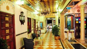 A hotel lobby with a checkered floor, ornate wall decorations, a chandelier, and a reception desk.