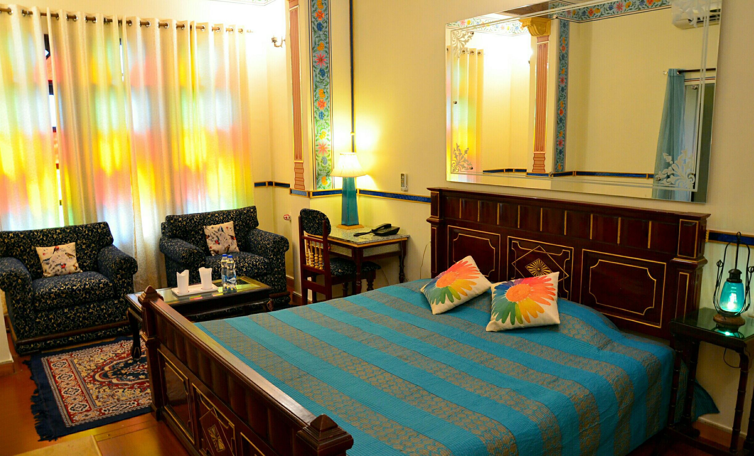 A hotel room with a bed, two armchairs, a small table, a lamp, and a mirror.