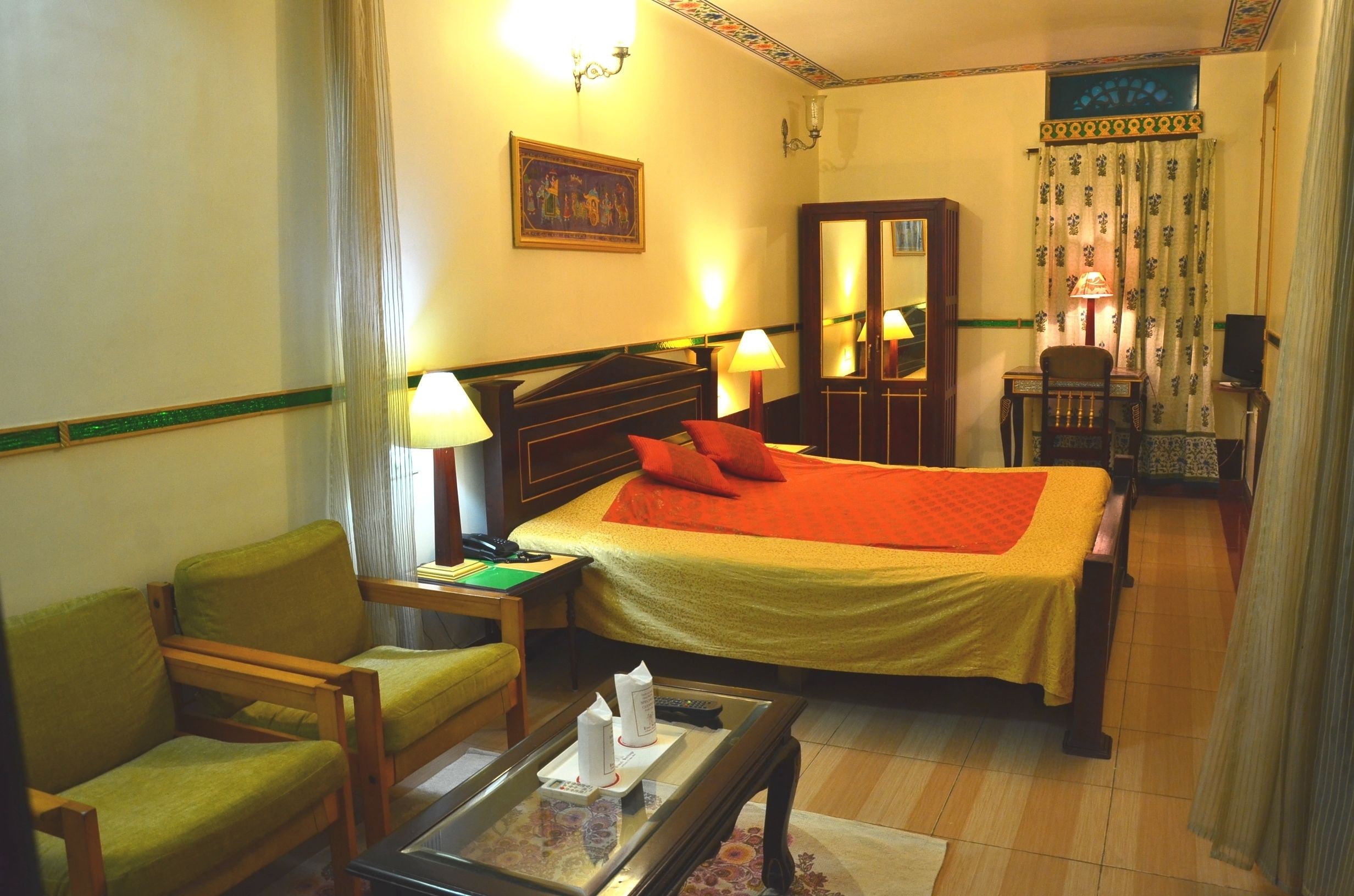 A hotel room with a bed, a chair, a desk, a lamp, and a mirror.