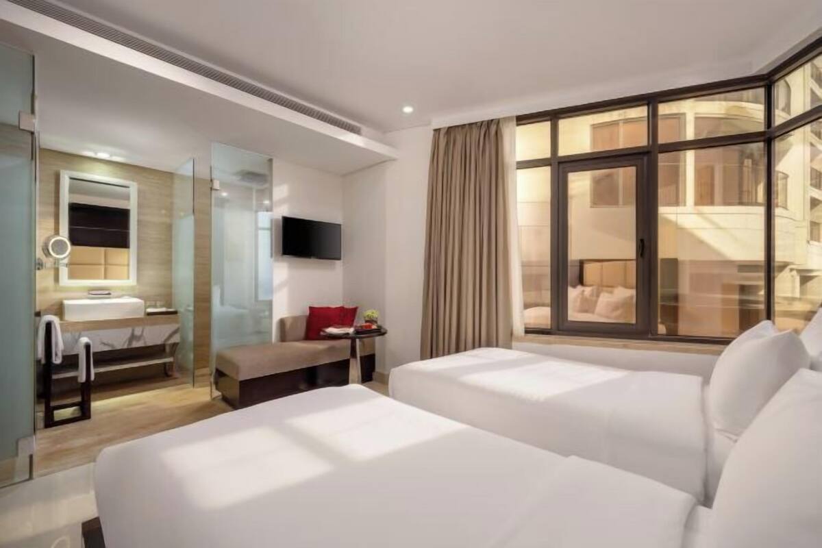 Une chambre d’hôtel avec deux lits, une télévision, une salle de bain avec un miroir et une fenêtre avec des rideaux.