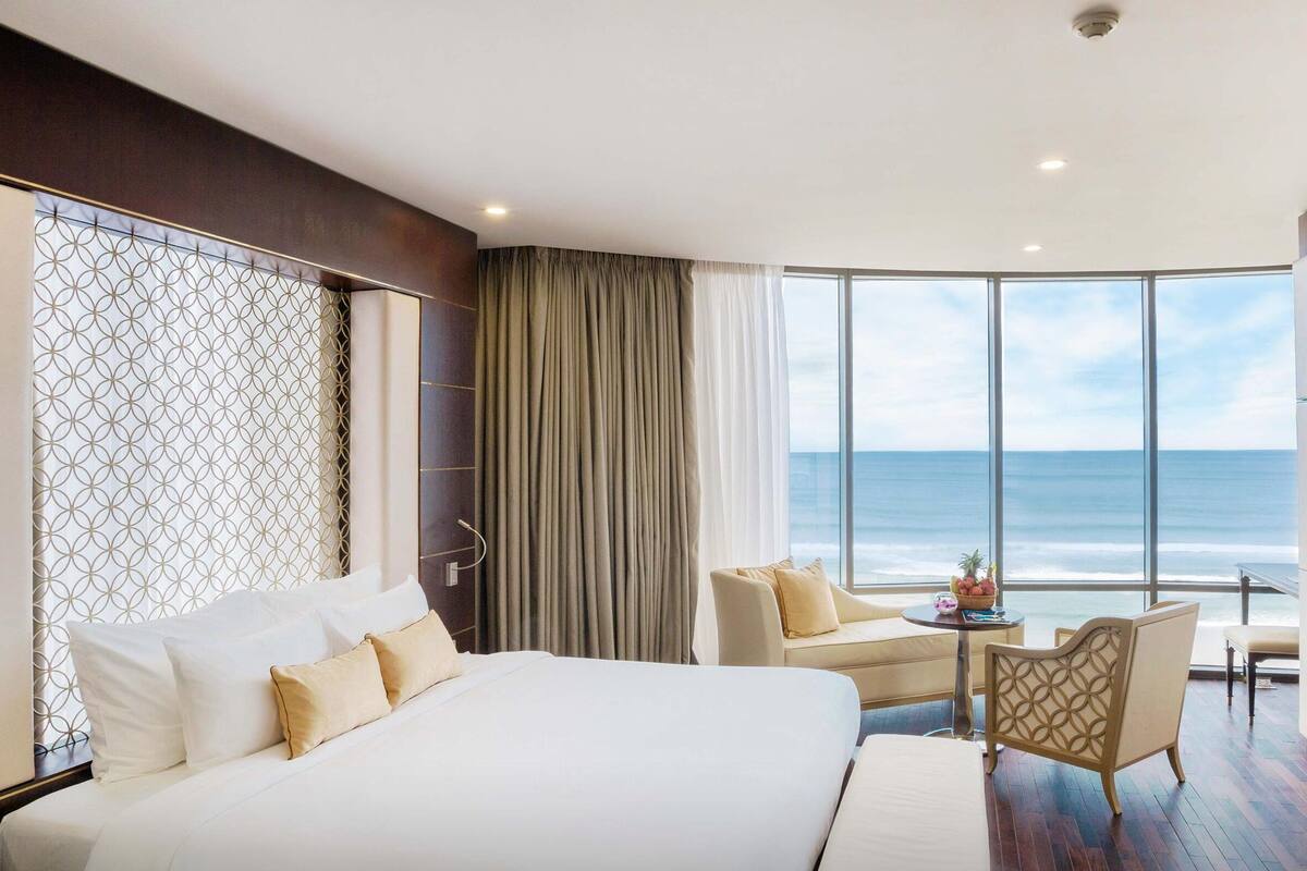 Une chambre d’hôtel avec un grand lit, un coin salon avec une table et une vue sur l’océan.