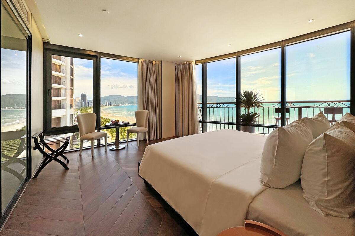 Une chambre d’hôtel dotée d’un grand lit, d’un balcon avec vue sur la mer et d’un coin salon avec une table et des chaises.