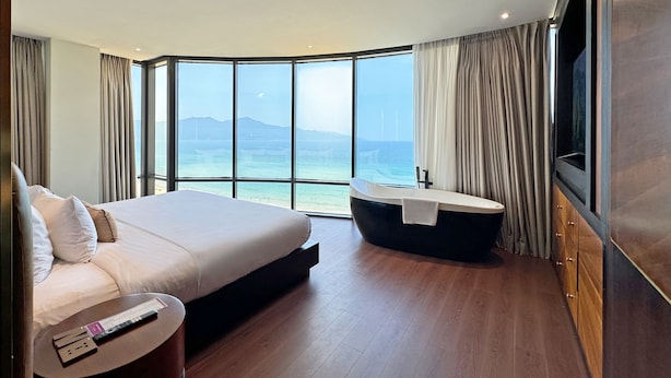A modern hotel room with a large bed, a bathtub, and a TV.