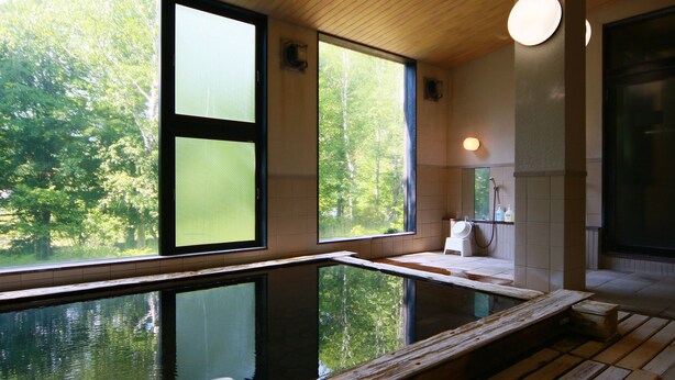 Een wellnessruimte met een houten terras, een whirlpool en grote ramen met uitzicht op bomen.