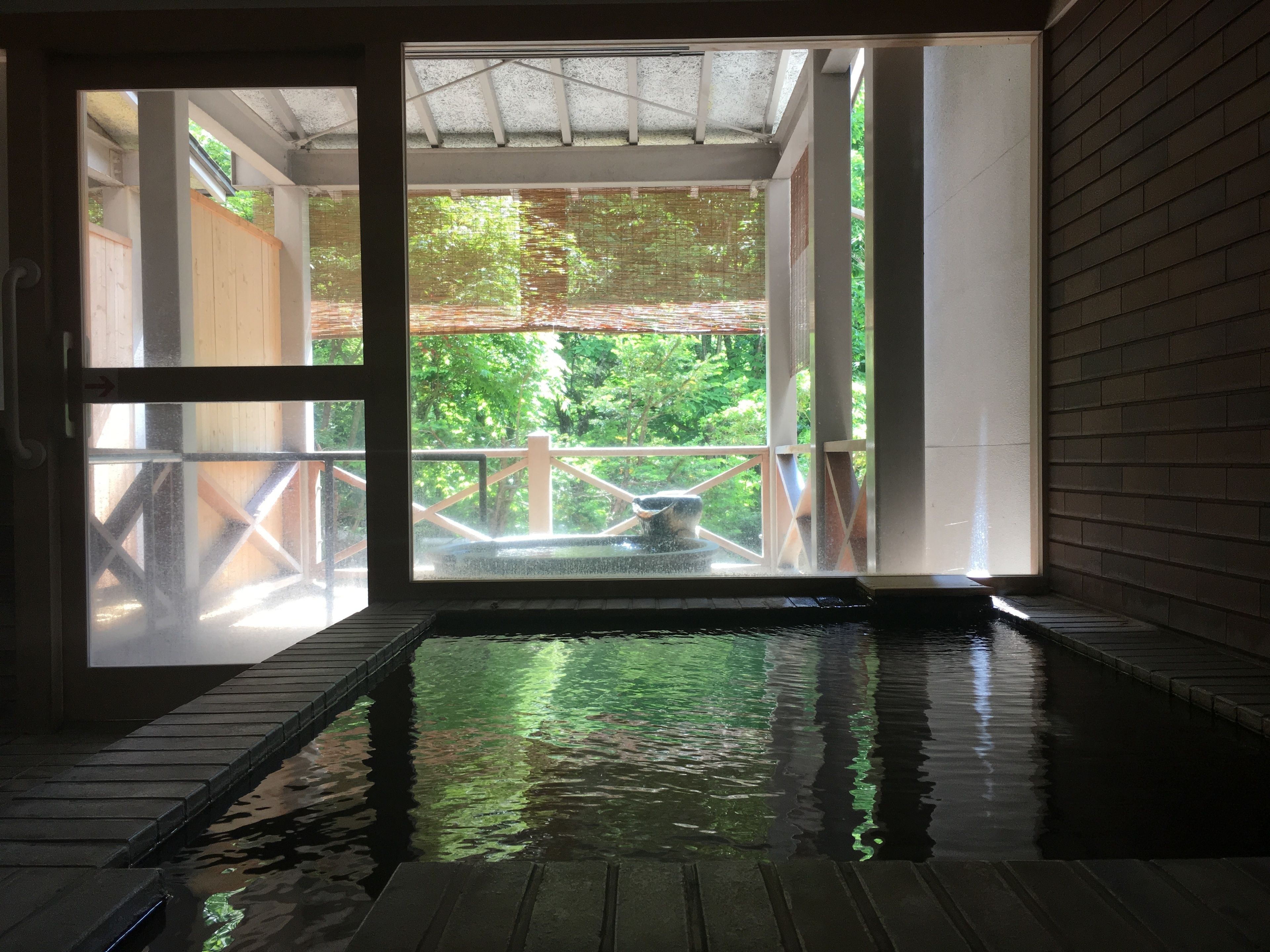 An indoor hot spring area with a wooden deck and a view of greenery outside.