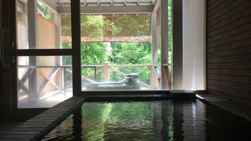 An indoor hot spring area with a wooden deck and a view of greenery outside.