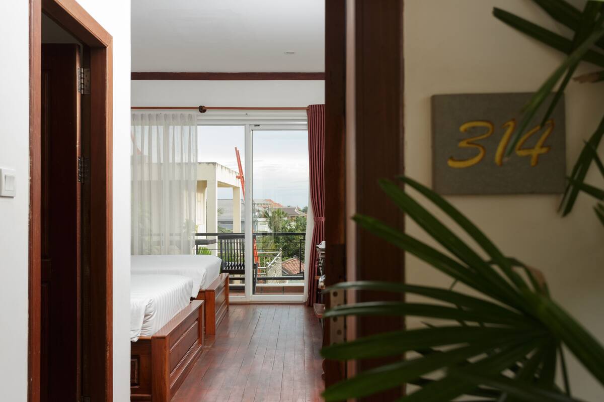Habitación de hotel con balcón, una cama, suelo de madera y un cartel con un número en la pared.