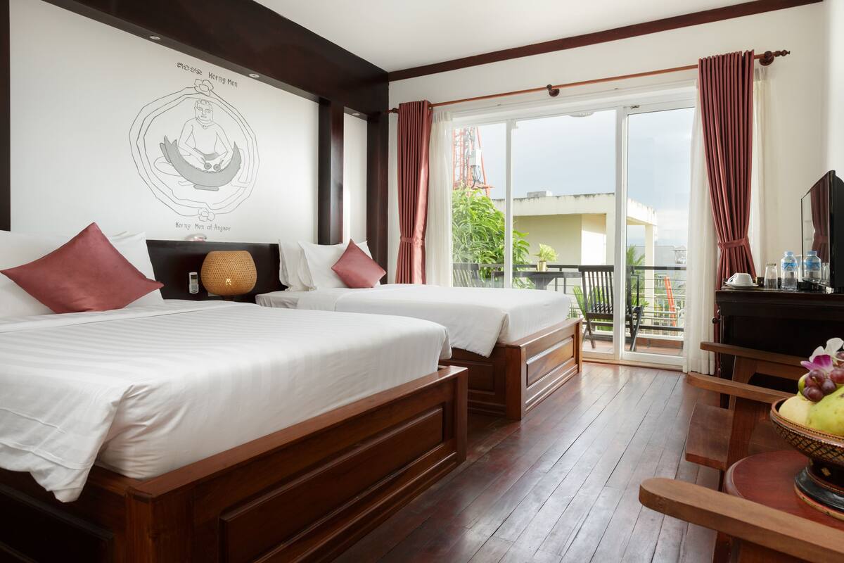 Habitación de hotel con dos camas de madera, un balcón con vistas y un área de comedor con un frutero.