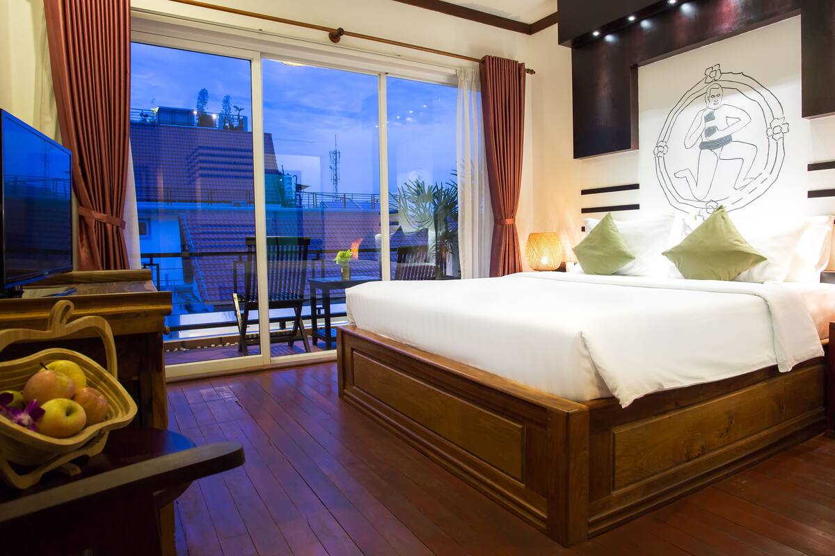 Una habitación de hotel con una cama grande, un televisor, un balcón con vistas a edificios y un adorno en la pared.